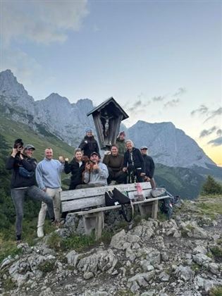Eine Gruppe von zehn Personen steht fröhlich auf einem Berg. Im Hintergrund sind beeindruckende Felsen und ein klarer Himmel zu sehen.