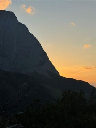 Ein majestätischer Berg im Hintergrund mit einem orangefarbenen Sonnenuntergang. Die Silhouette des Berges hebt sich gegen den Himmel ab.