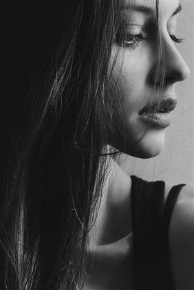 Ein Porträt einer Frau in Schwarz-Weiß, das ihr Profil zeigt. Ihr Haar fällt sanft über die Schulter und sie hat einen nachdenklichen Ausdruck.