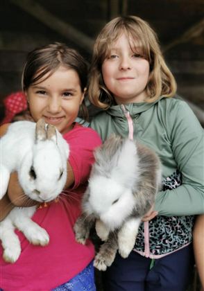 Zwei Mädchen halten liebevoll Kaninchen in ihren Armen. Sie lächeln glücklich in die Kamera.