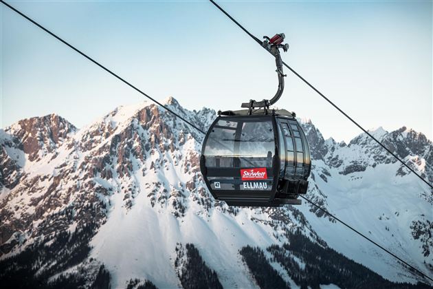 Eine Seilbahn schwebt über schneebedeckte Berge. Der Himmel ist klar und die Landschaft wirkt majestätisch.