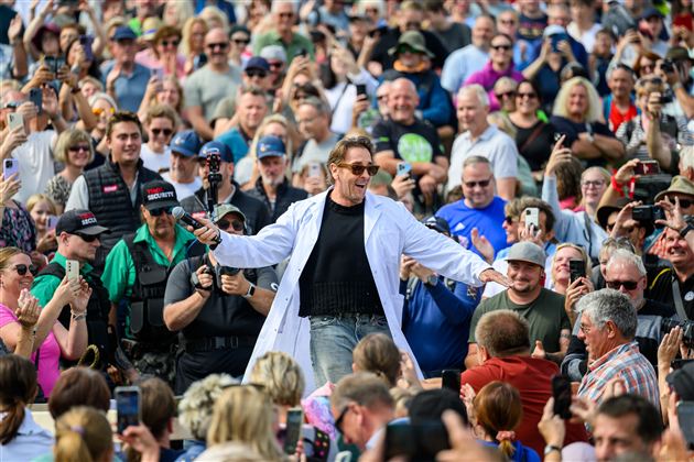 Ein Mann in einem weißen Laborkittel steht im Mittelpunkt einer großen Menschenmenge. Die Zuschauer applaudieren und nehmen Fotos auf.