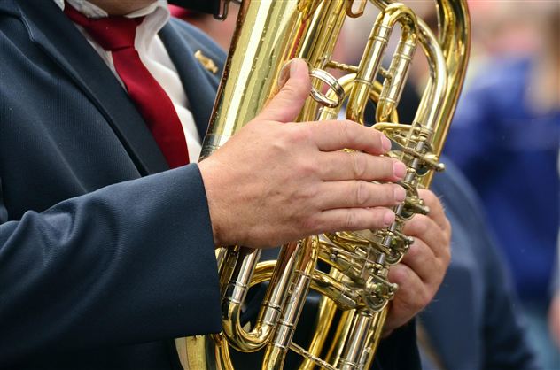 Ein Musiker hält eine glänzende Tuba in den Händen. Er trägt einen Anzug mit einer roten Krawatte.