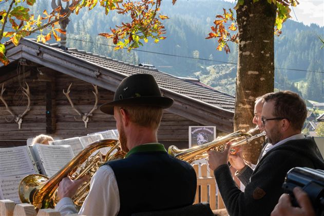 Eine Person spielt auf einem Akkordeon, während sie traditionelle bayerische Tracht trägt. Im Hintergrund sind weitere Musiker zu sehen.