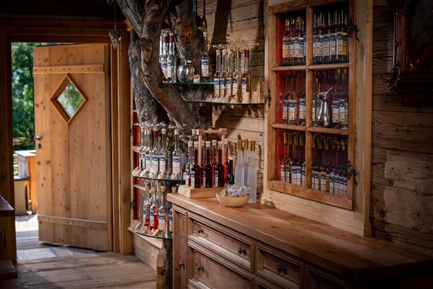 Ein gemütlicher Raum mit Holzmöbeln und einer offenen Tür. An der Wand sind viele Flaschen mit verschiedenen Getränken ausgestellt.