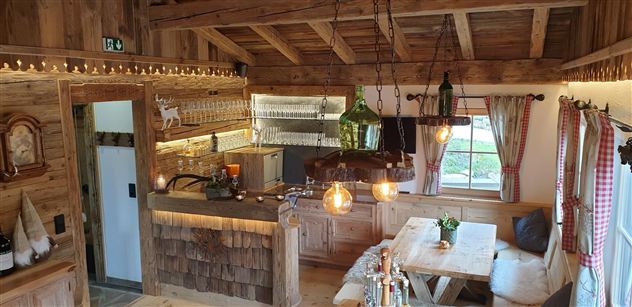 Eine gemütliche Holzstube mit einer großzügigen Theke und einem großen Esstisch. Warmes Licht und rustikale Dekoration schaffen eine einladende Atmosphäre.