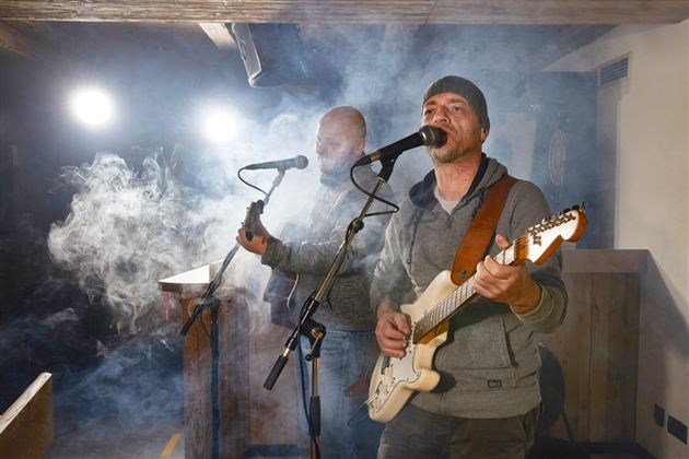 Zwei Musiker treten auf einer Bühne auf und spielen akustische Gitarre. Nebel und Scheinwerferlicht schaffen eine stimmungsvolle Atmosphäre.