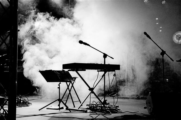Eine musikalische Bühne mit einem Keyboard und Mikrophonen. Der Raum ist von Nebel umhüllt und schafft eine mystische Atmosphäre.