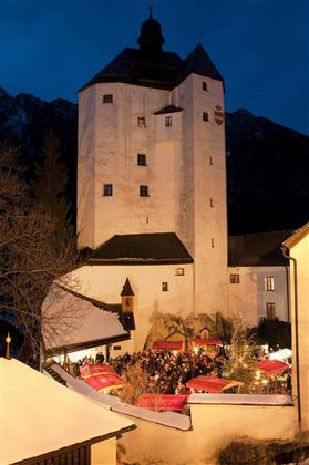 Een historische toren bij nacht, omringd door feestelijke verlichting. Veel mensen verzamelen zich om deel te nemen aan een markt.