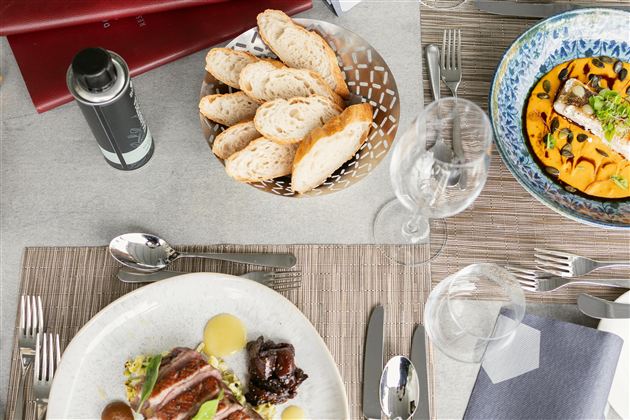 Ein eleganter Tisch gedeckt mit verschiedenen Gerichten und frischem Brot. Im Hintergrund sind Gläser und Besteck zu sehen.