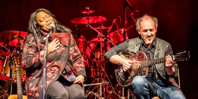 Zwei Musiker treten auf einer Bühne auf. Die Sängerin hält ein Mikrofon und singt, während der Gitarrist spielt.