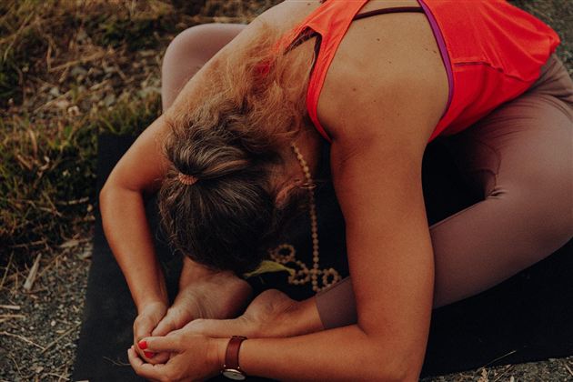Eine Person macht eine Yoga-Übung auf einer Matte im Freien. Sie beugt sich vor und hält einen Fuß.