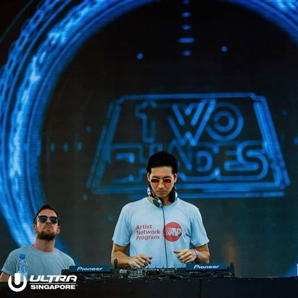 Ein DJ steht an einem Mischpult auf einer Bühne. Im Hintergrund ist ein großes LED-Display mit dem Schriftzug "TWO SHADES" zu sehen.