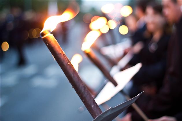 Eine Gruppe von Menschen hält Fackeln in der Dämmerung. Die Flammen leuchten in der Dunkelheit und schaffen eine feierliche Atmosphäre.