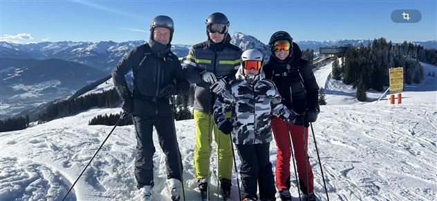 Eine Gruppe von vier Skifahrern steht auf einem schneebedeckten Hang. Im Hintergrund sind Berge und ein klarer Himmel zu sehen.