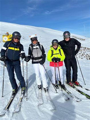 Eine Gruppe von vier Skifahrern steht auf einer verschneiten Piste. Der Himmel ist klar und blau.