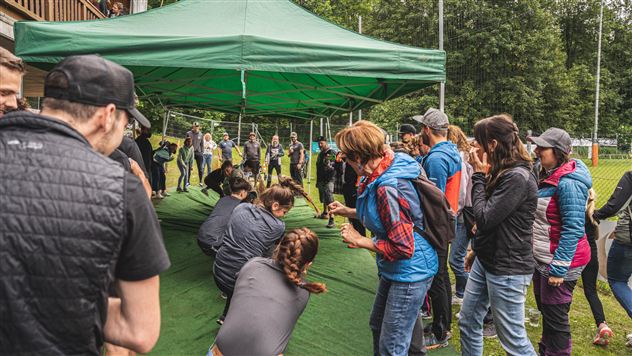 Eine Gruppe von Menschen versammelt sich unter einem grünen Zelt. Sie interagieren und scheinen an einer Aktivität teilzunehmen.
