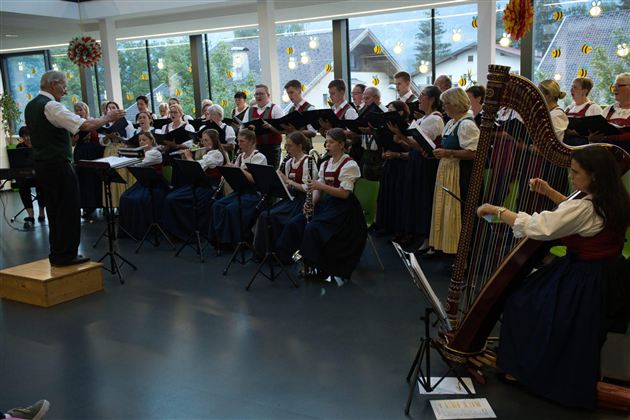 En kor i traditionelle dragter synger under ledelse af en dirigent. I forgrunden ses en harpe.