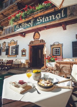 Ein einladendes Gasthaus mit einem schönen Außenbereich und blühenden Blumen. Auf dem Tisch stehen Frühstücksteller und Getränke bereit.