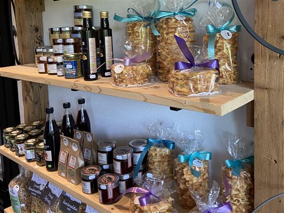 Ein Holztisch mit Regalen voller Lebensmittelprodukte. Es gibt Flaschen, Marmelade und hübsch verpackte Süßigkeiten mit bunten Schleifen.