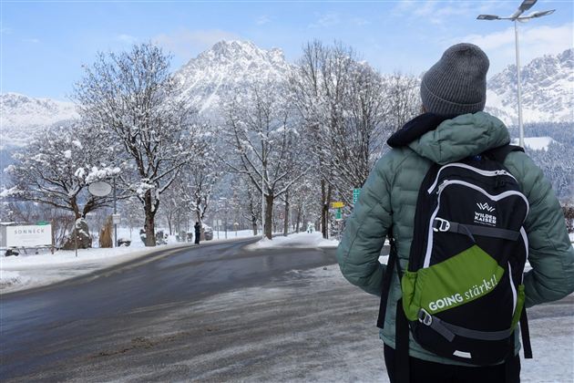 Eine Person steht an einer schneebedeckten Straße und schaut auf die Berge. Umgeben von verschneiten Bäumen, ist die Szenerie ruhig und winterlich.