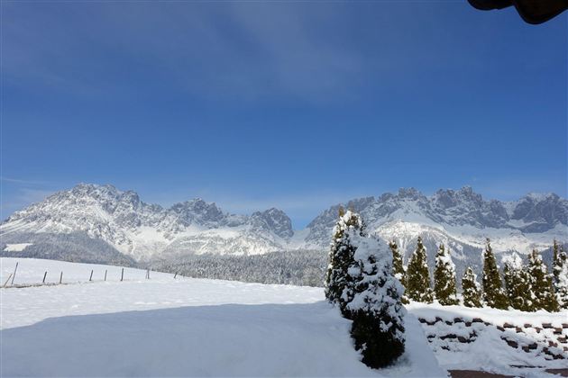 Eine schneebedeckte Landschaft mit majestätischen Bergen im Hintergrund. Der Himmel ist klar und strahlend blau.