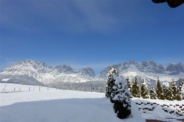 Een met sneeuw bedekt landschap met majestueuze bergen op de achtergrond. De lucht is helder en stralend blauw.