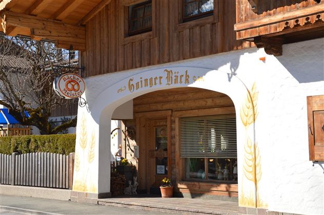 Ein charmantes Holzgebäude mit einem einladenden Eingang. Über der Tür steht "Ginger Bäck" und es gibt dekorative Elemente wie Ähren an der Wand.