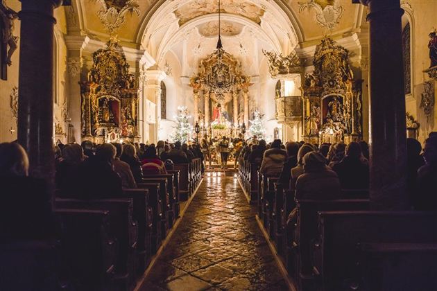 Eine besinnliche Kirche mit einer vollen Bankreihe und festlicher Beleuchtung. Im Hintergrund ist ein wunderschön dekorierter Altar zu sehen.