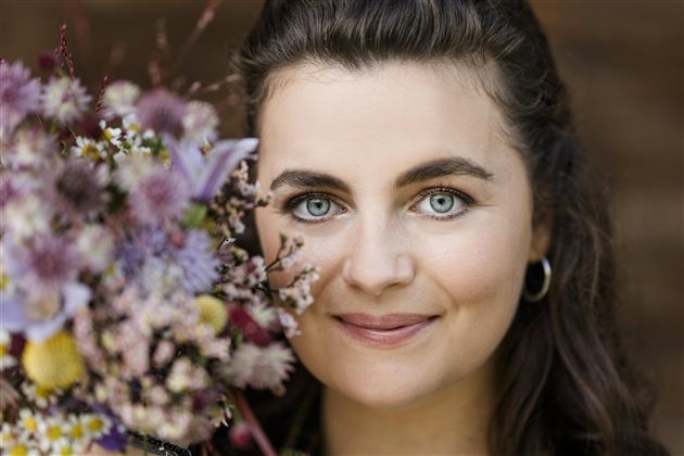 A woman holds a colorful bouquet of flowers and smiles. Her gaze is friendly and her eyes shine.