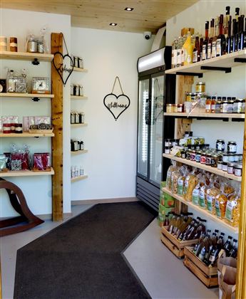 Ein Laden mit verschiedenen Regalen voller Lebensmittel und Getränken. Auf der linken Seite sind Gläser und Flaschen ausgestellt, während rechts ein Kühlschrank und weitere Waren stehen.