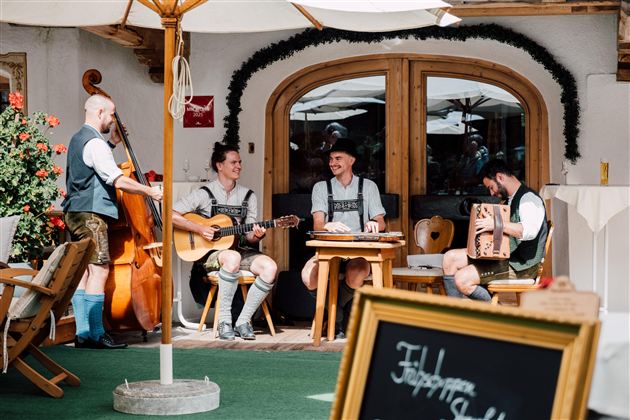 Eine Gruppe von Musikern in traditioneller Tracht spielt in einem gemütlichen Außenbereich. Die Atmosphäre ist entspannt und einladend.