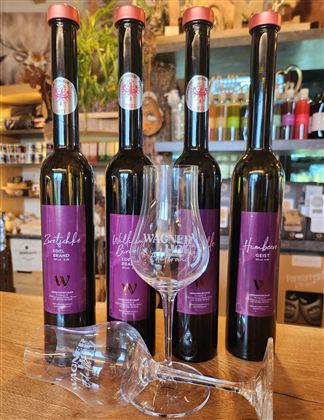 Vier Flaschen mit Wein, die nebeneinander stehen, und ein Weinglas im Vordergrund. Die Etiketten sind in lila gehalten und enthalten verschiedene Namen.