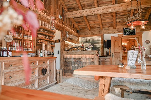 Eine gemütliche Holzbar mit einem einladenden Interieur. Im Hintergrund sind Regale mit Getränken und eine schöne Theke zu sehen.