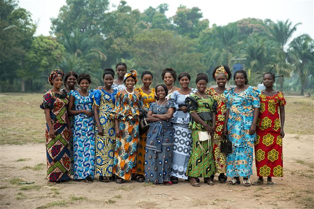 Eine Gruppe von Frauen in bunten traditionellen Kleidern steht in einem Park. Im Hintergrund sind Bäume und eine grüne Landschaft zu sehen.