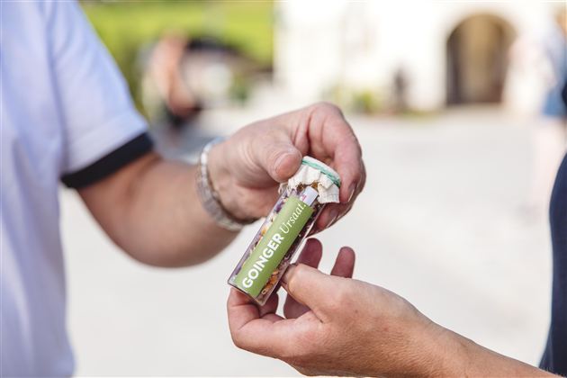 Ein Landwirt steht in einem Feld und überprüft die Pflanzen. Im Hintergrund sind Bäume und sanfte Hügel zu sehen.