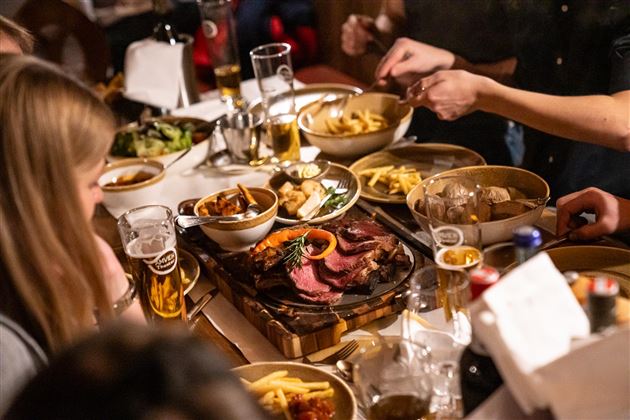 Ein gemütliches Essen mit Freunden, das verschiedene Gerichte und Getränke umfasst. Auf dem Tisch liegen Fleisch, Beilagen und Salat.
