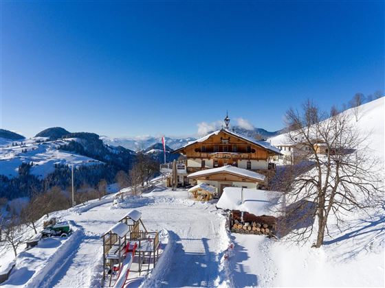 Ein malerisches Bergdorf im Schnee mit einer gemütlichen Hütte. Der Himmel ist klar und blau, umgeben von schneebedeckten Hügeln.