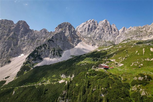 Eine beeindruckende Berglandschaft mit hohen Felsen und grünen Wiesen. Im Vordergrund befindet sich ein rotes Haus in der idyllischen Natur.