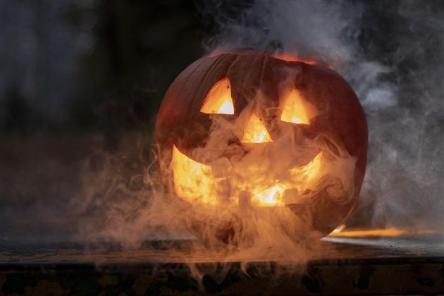 Ein leuchtender Kürbis mit fröhlichem Gesicht steht vor einer nebligen Kulisse. Der Kürbis ist Teil der Halloween-Dekoration.