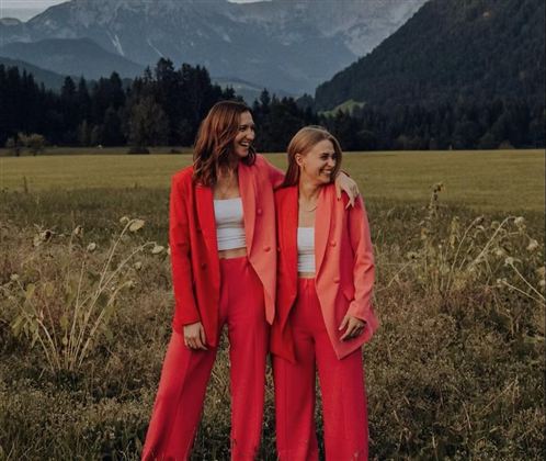 Ein Musiker spielt akustische Gitarre und singt in einem Freiluftbereich. Im Hintergrund sind Menschen und eine schöne Landschaft zu sehen.