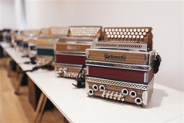 A group of people is playing traditional music with an accordion. They are wearing Bavarian costumes and sitting outdoors.