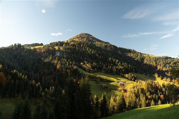 Zwei Radfahrer stehen auf einer Wiese und blicken auf eine wunderschöne Berglandschaft. Die Sonne geht gerade unter und schafft eine malerische Atmosphäre.