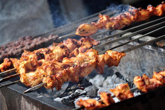 Gegrillte Spieße mit Fleisch und Gemüse über glühenden Kohlen. Dicht stehender Rauch umgibt die Grillfläche.