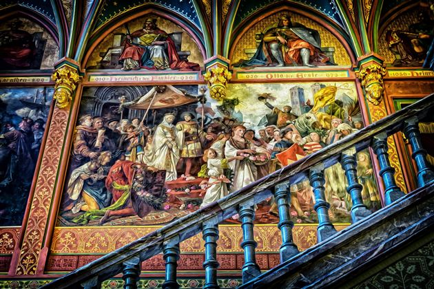 Ein prachtvoller Wandteppich mit historischen Szenen und lebendigen Farben. Eine Treppe führt hinunter, umgeben von detaillierten Malereien.
