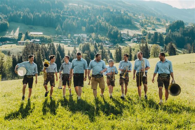 Een groep mannen in Beierse klederdracht marcheert over een groene weide. Op de achtergrond zijn bergen en bossen te zien.