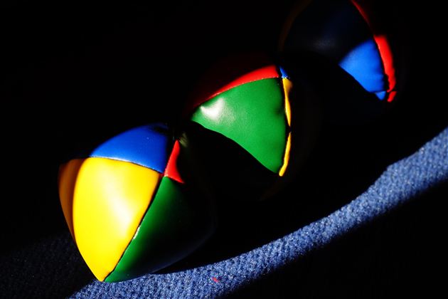 Drei bunte Jonglierbälle liegen auf einem Teppich. Sie haben leuchtende Farben in Blau, Grün, Gelb und Rot.
