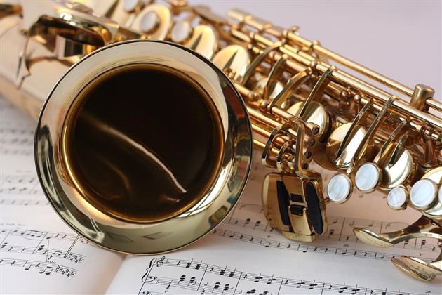 Lesklý saxofon leží na notovém papíře. Detaily kláves jsou dobře viditelné.