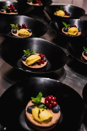 Eine elegante Dessertpräsentation in schwarzen Schalen. Die Desserts sind mit Beeren und einer gelben Sorbetkugel dekoriert.