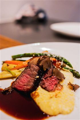 Ein Teller mit zartem Rindfleisch, serviert auf cremigem Kartoffelpüree. Daneben liegen frisches Gemüse und eine dunkle Sauce.